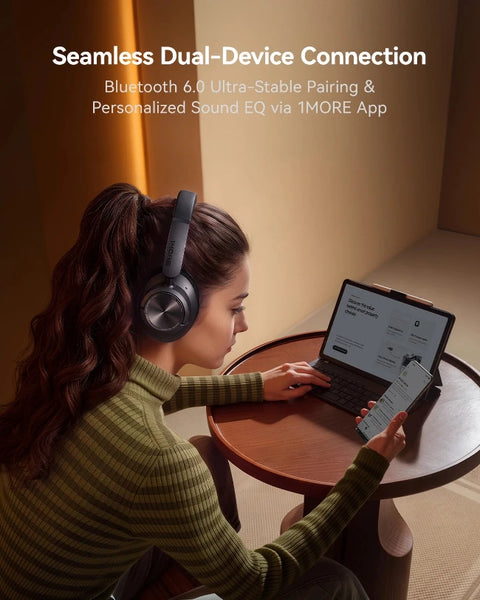 A woman wearing over-ear headphones sits at a small wooden table, using a tablet and holding a phone. Text at the top reads 'Seamless Dual-Device Connection' with Bluetooth 6.